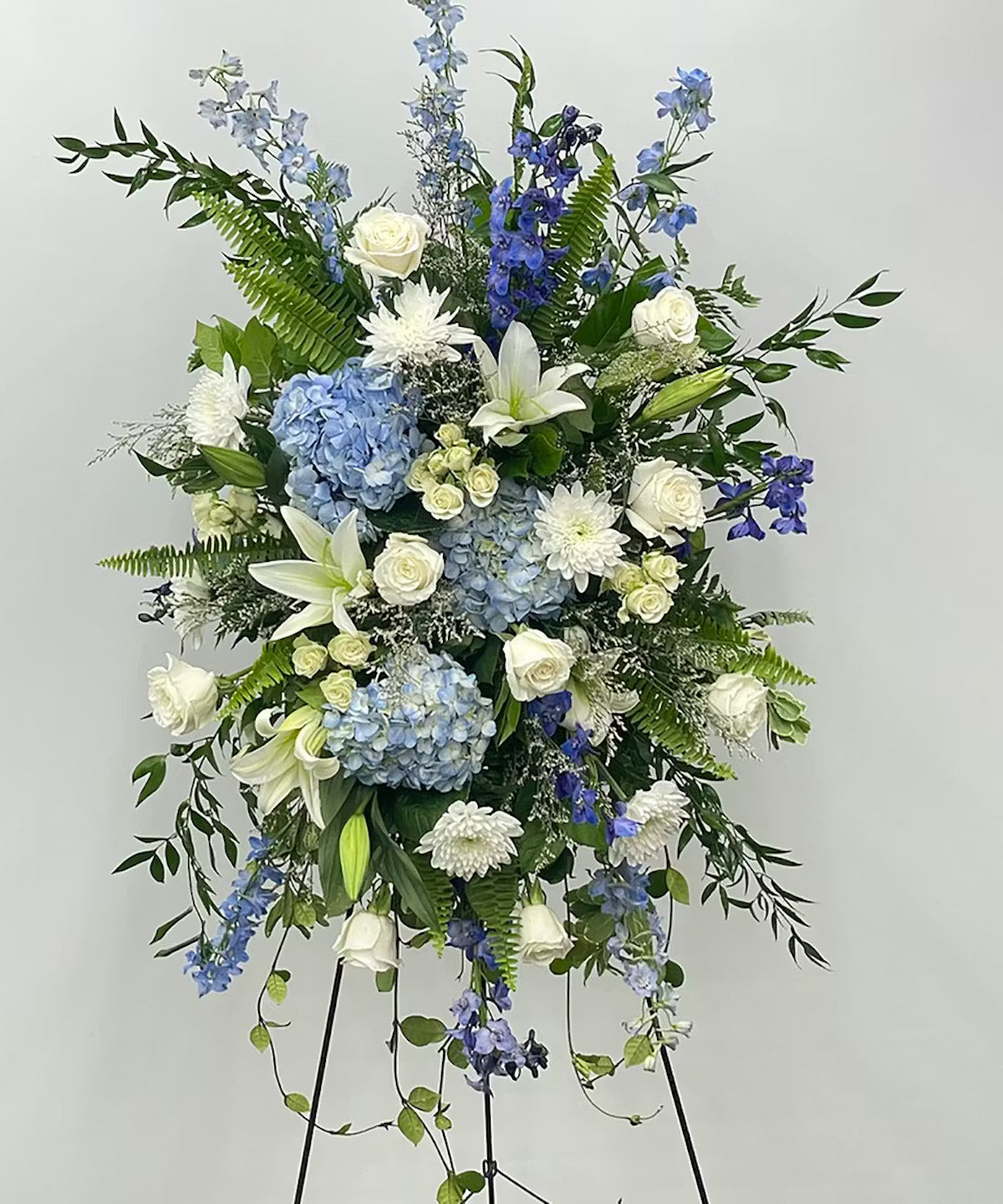 A large standing spray of funeral flowers made of green, white, and blue flowers.