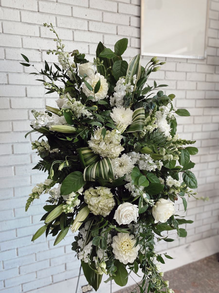 A large standing spray of funeral flowers made of green and white flowers.