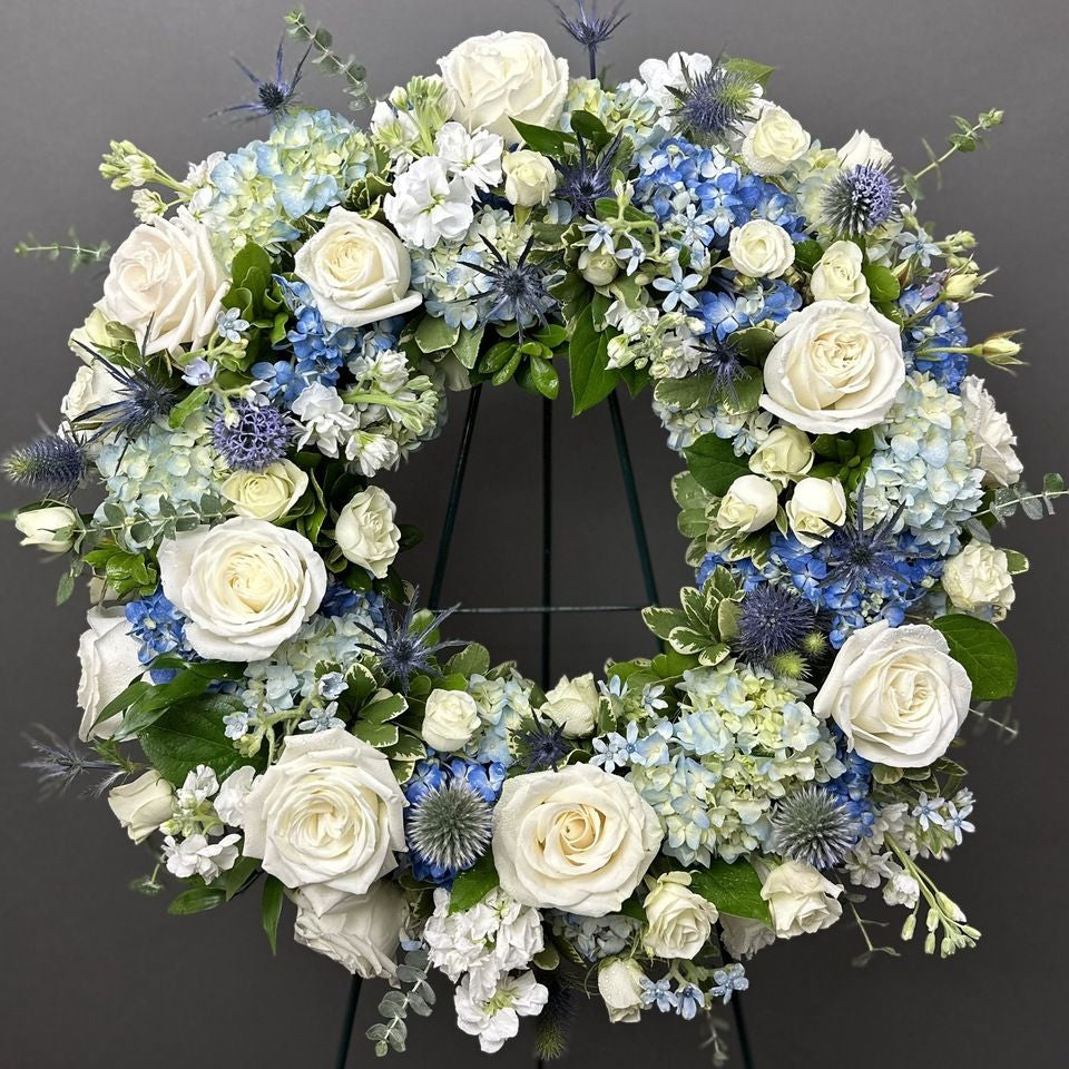 A floral wreath made of green, blue, and white flowers for a standing funeral spray.
