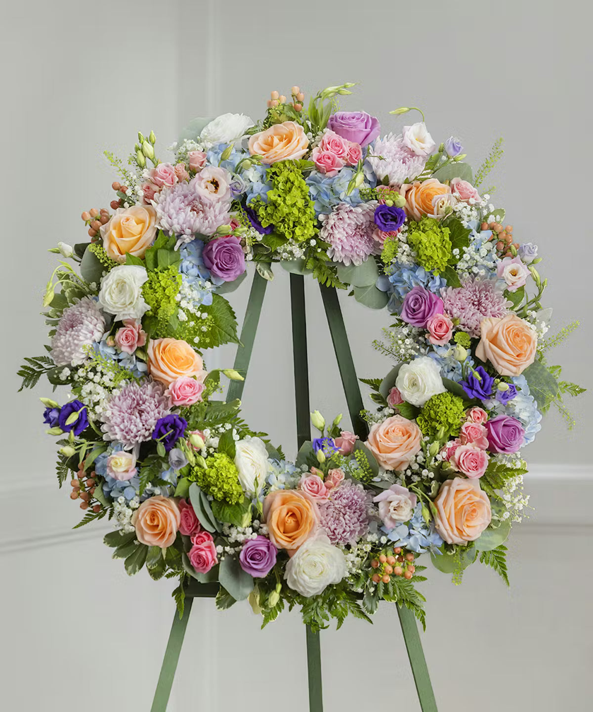 A floral wreath made of pastel flowers, using green, white, pink, purple, and orange flowers for a standing funeral spray.