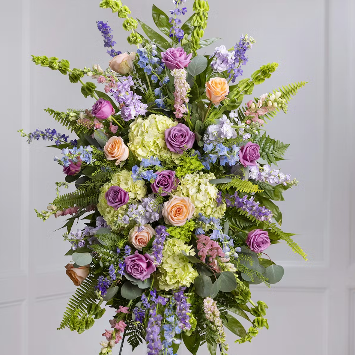 A large standing spray of funeral flowers made of pastel colors like purple, green, orange, and blue.
