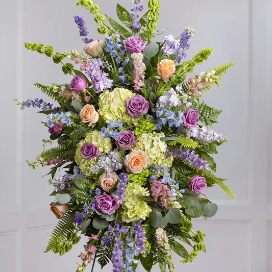 A large standing spray of funeral flowers made of pastel colors like purple, green, orange, and blue.