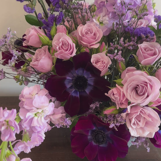 A video of a pink and purple flower arrangement in a black vase. 