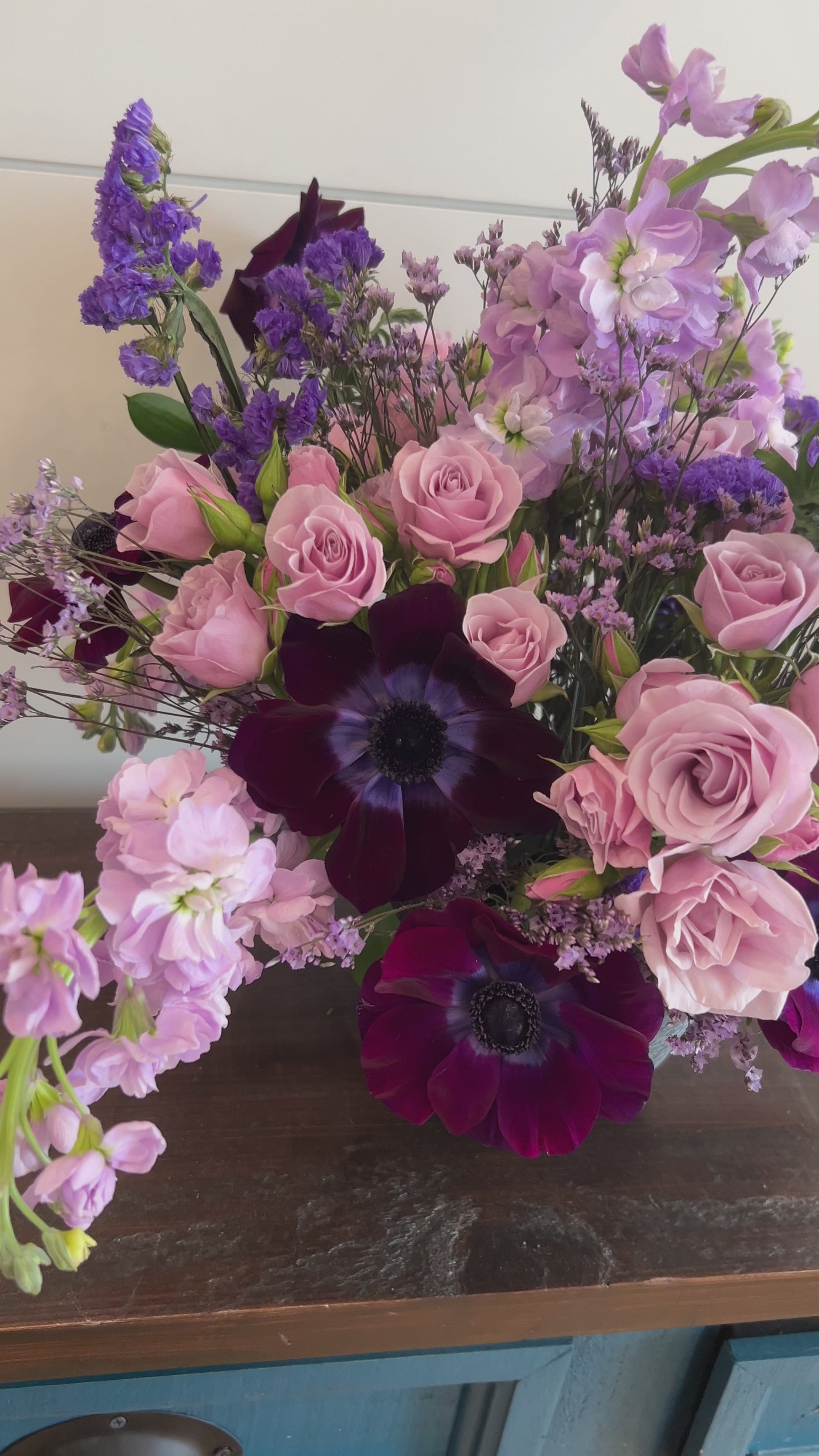A video of a pink and purple flower arrangement in a black vase. 