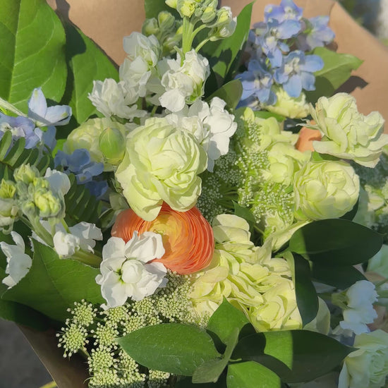A video of a bouquet of green, white, peach, and blue colored flowers.