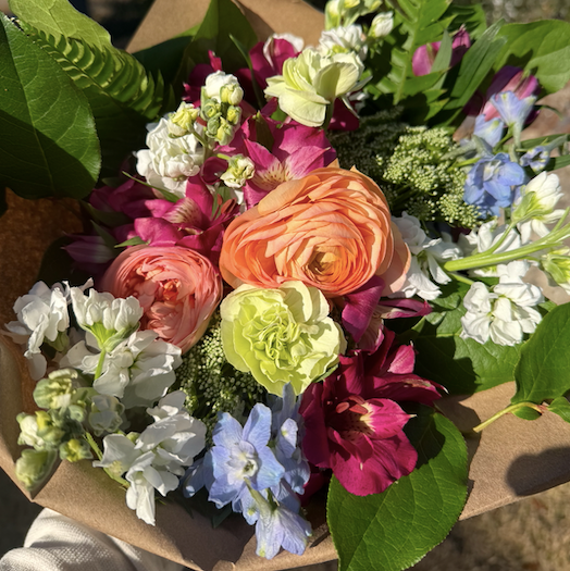 Bouquet of colorful flowers in a brown paper wrap held by a person outdoors.